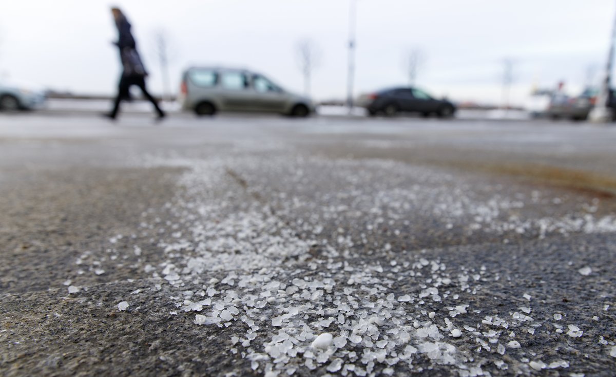 Close up of road salt on a sidewalk, cars and person walking in background.