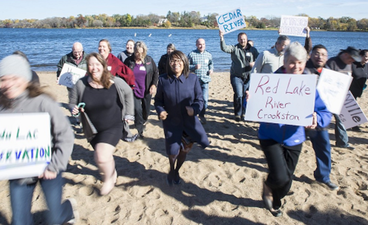 People holding signs joyfully running away from a lake